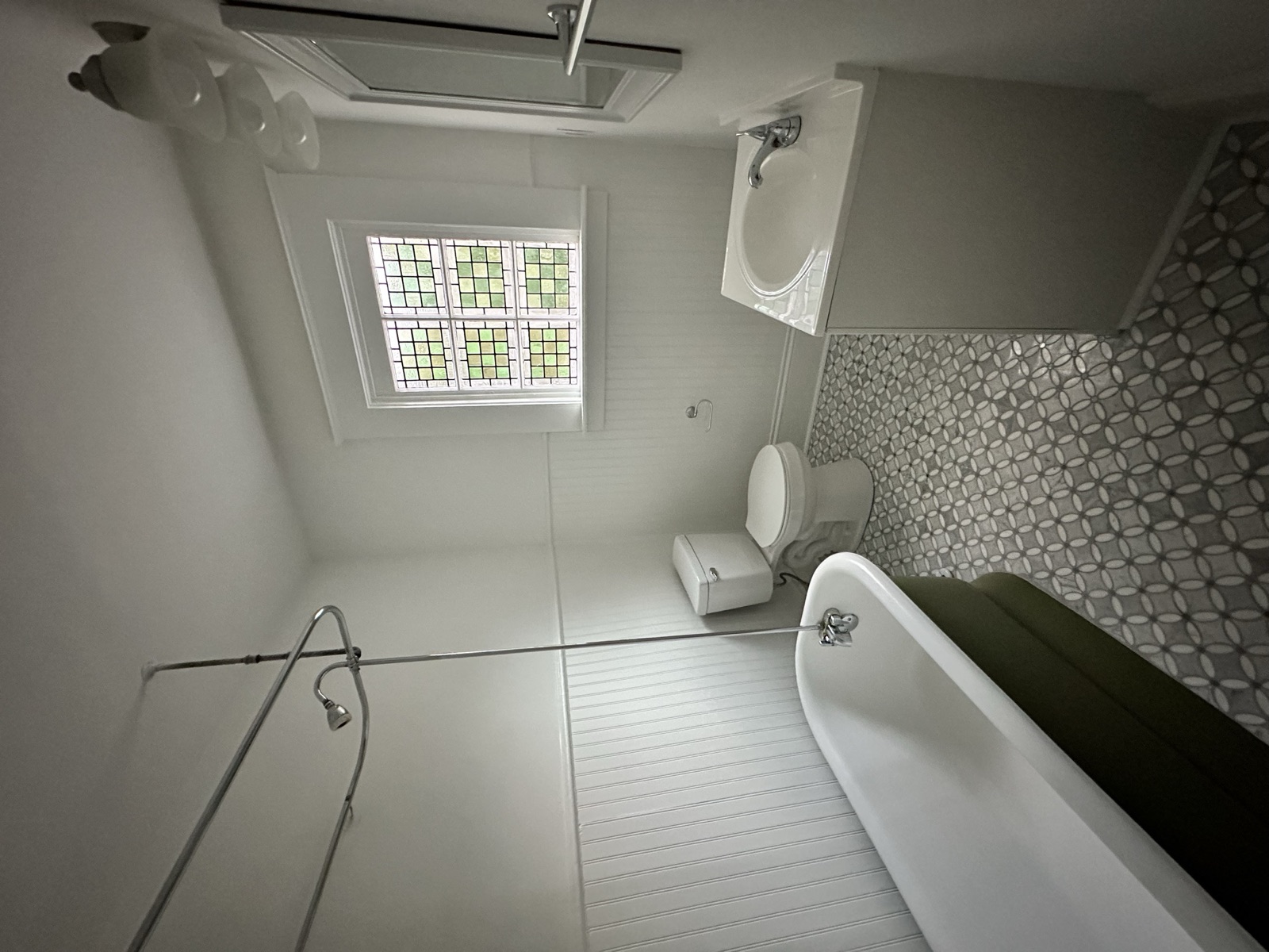 Bathroom with an olive-green painted tub, marble mosaic floor, beadboard wainscot, and a green stained-glass window